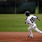 A young baseball player in uniform sprints towards base on a sunny day.