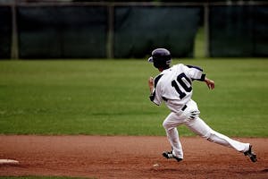 A young baseball player in uniform sprints towards base on a sunny day.