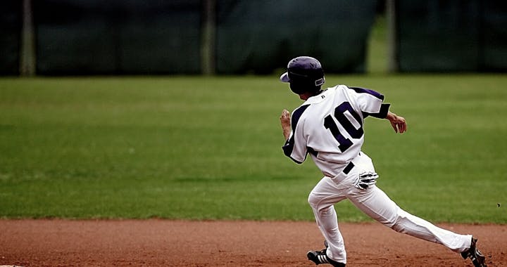 A young baseball player in uniform sprints towards base on a sunny day.