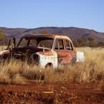 Vintage car decaying in a dry desert landscape with mountains in the background.
