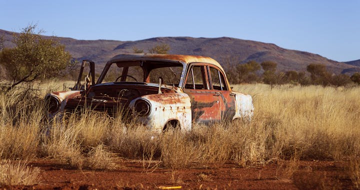 Vintage car decaying in a dry desert landscape with mountains in the background.