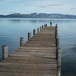 Distant traveler standing in solitude on long wooden pier with landscape of calm lake in highlands